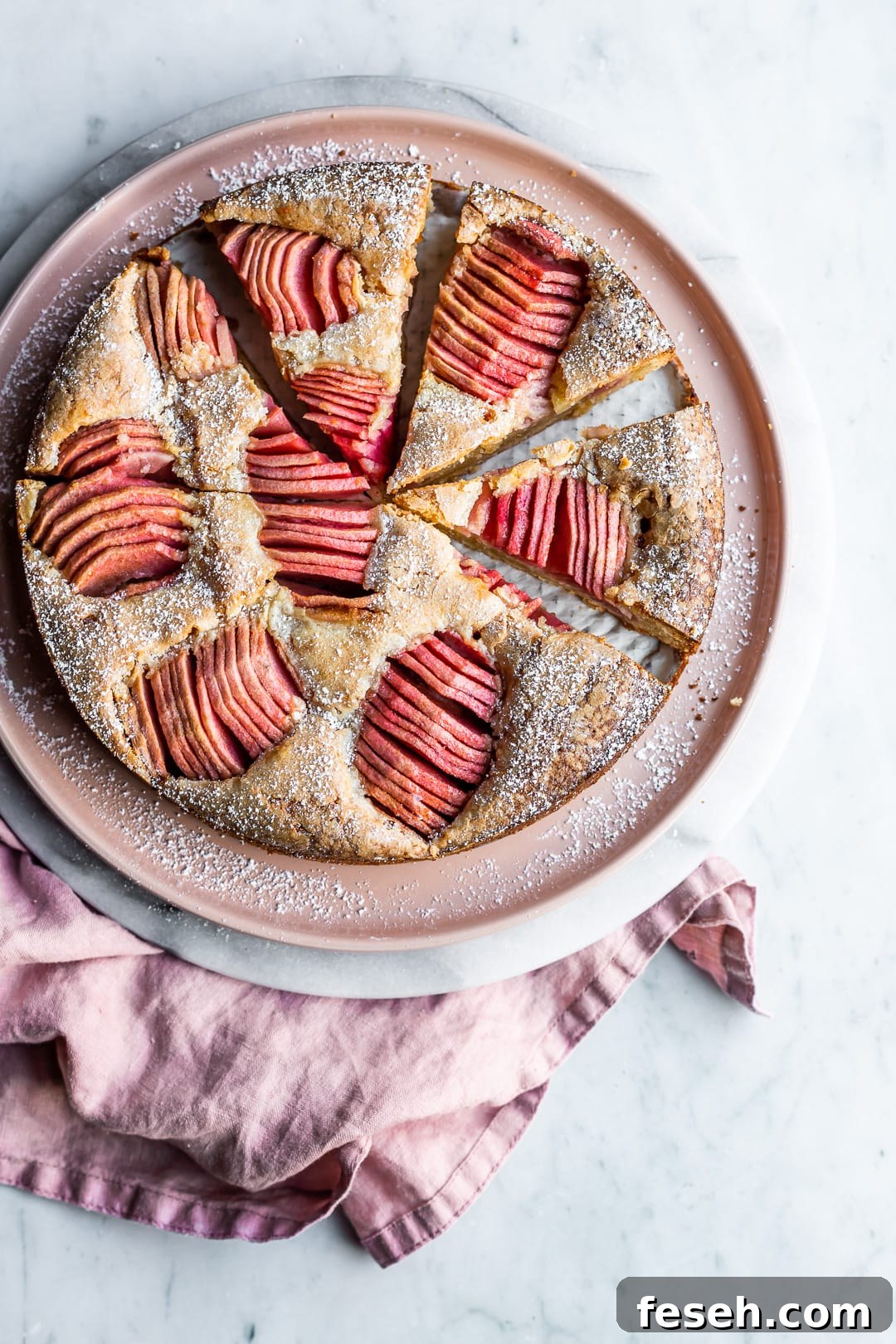 Sliced almond cake with pink apples on pink plate and marble surface