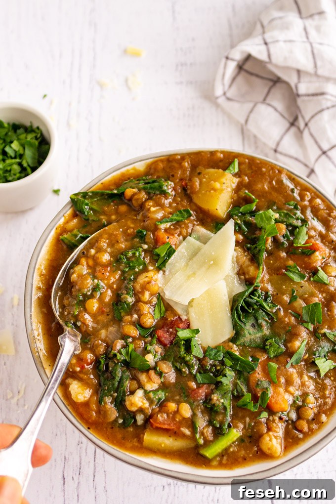 Side view of lentil soup in a white bowl with a hand holding a spoon.