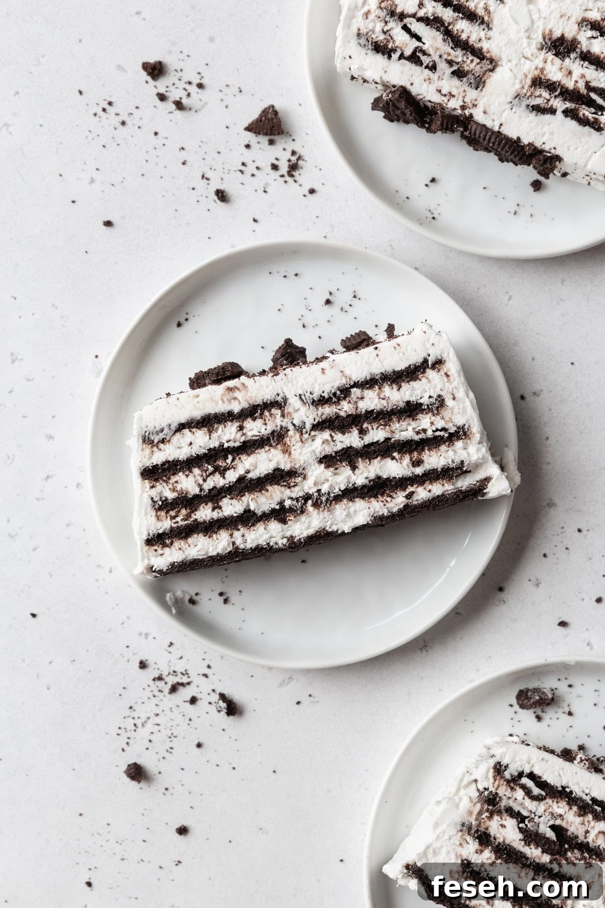 Three slices of icebox cake on white plates on a light grey surface.