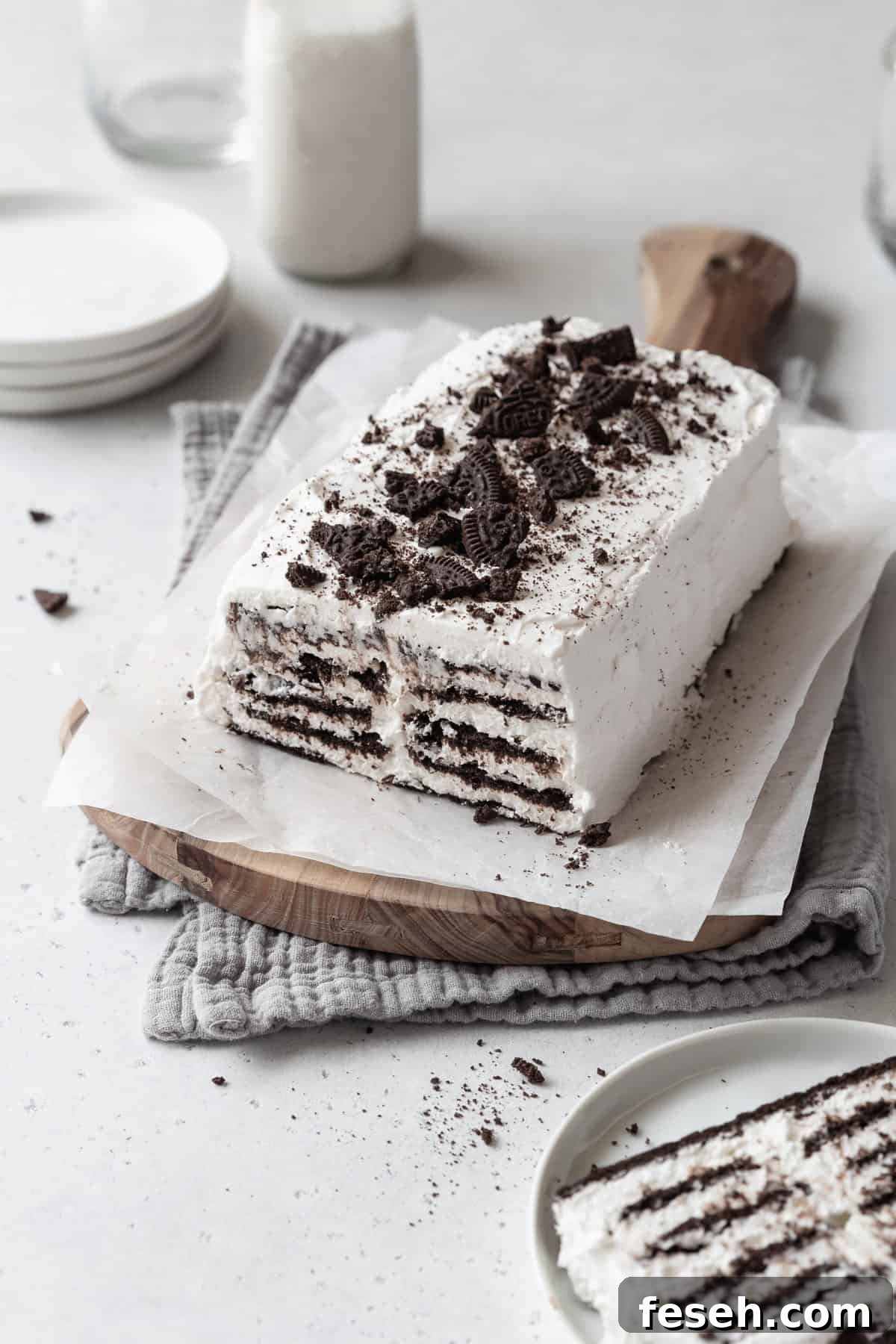 A loaf of icebox cake with cookie crumbs on top on a parchment paper lined wooden board. 