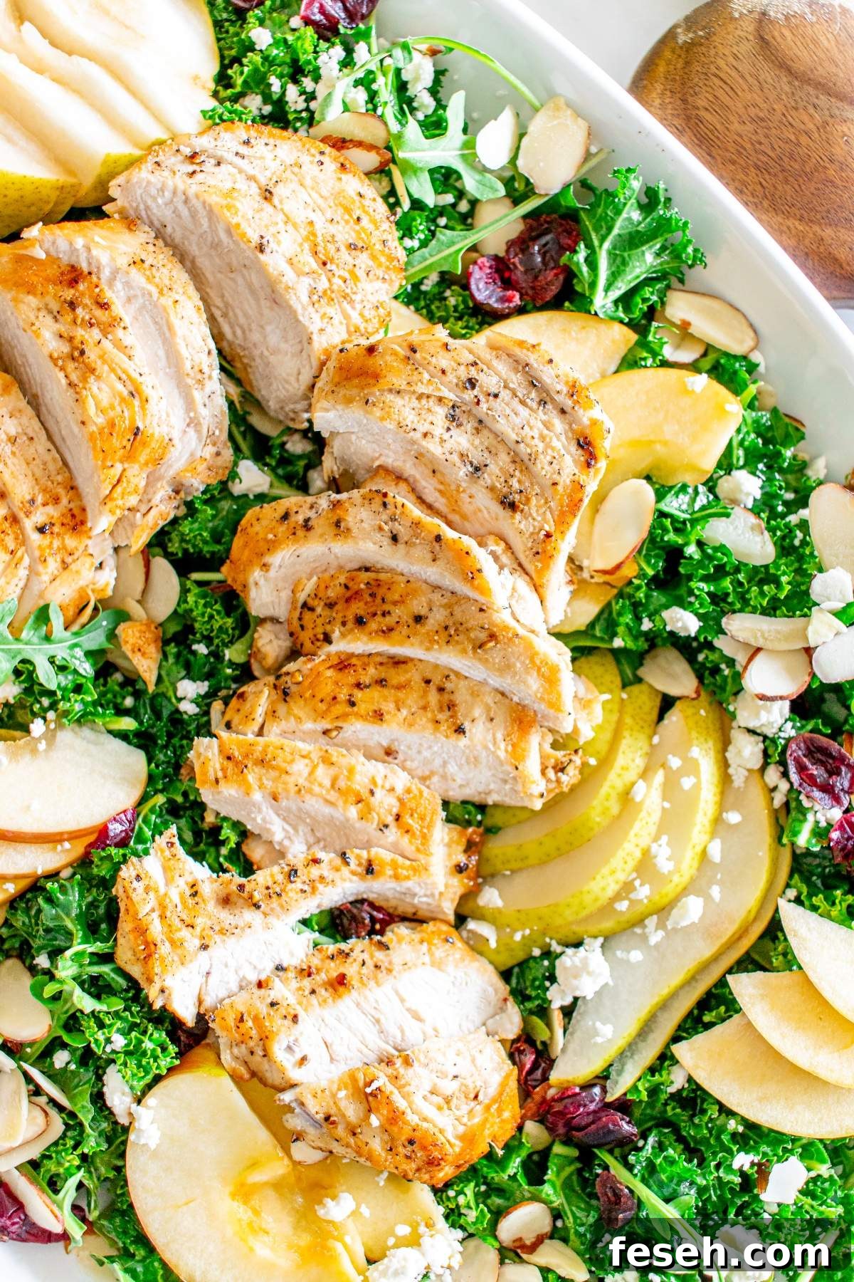 An autumn crunch salad with chicken, featuring sliced grilled chicken breast, apple and pear slices, feta cheese, almonds, and cranberries on a bed of mixed greens.