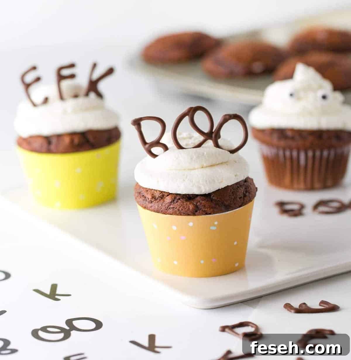 Chocolate cupcake with vanilla frosting in orange cupcake wrapper. With chocolate BOO word on top for edible Halloween cupcake topper.