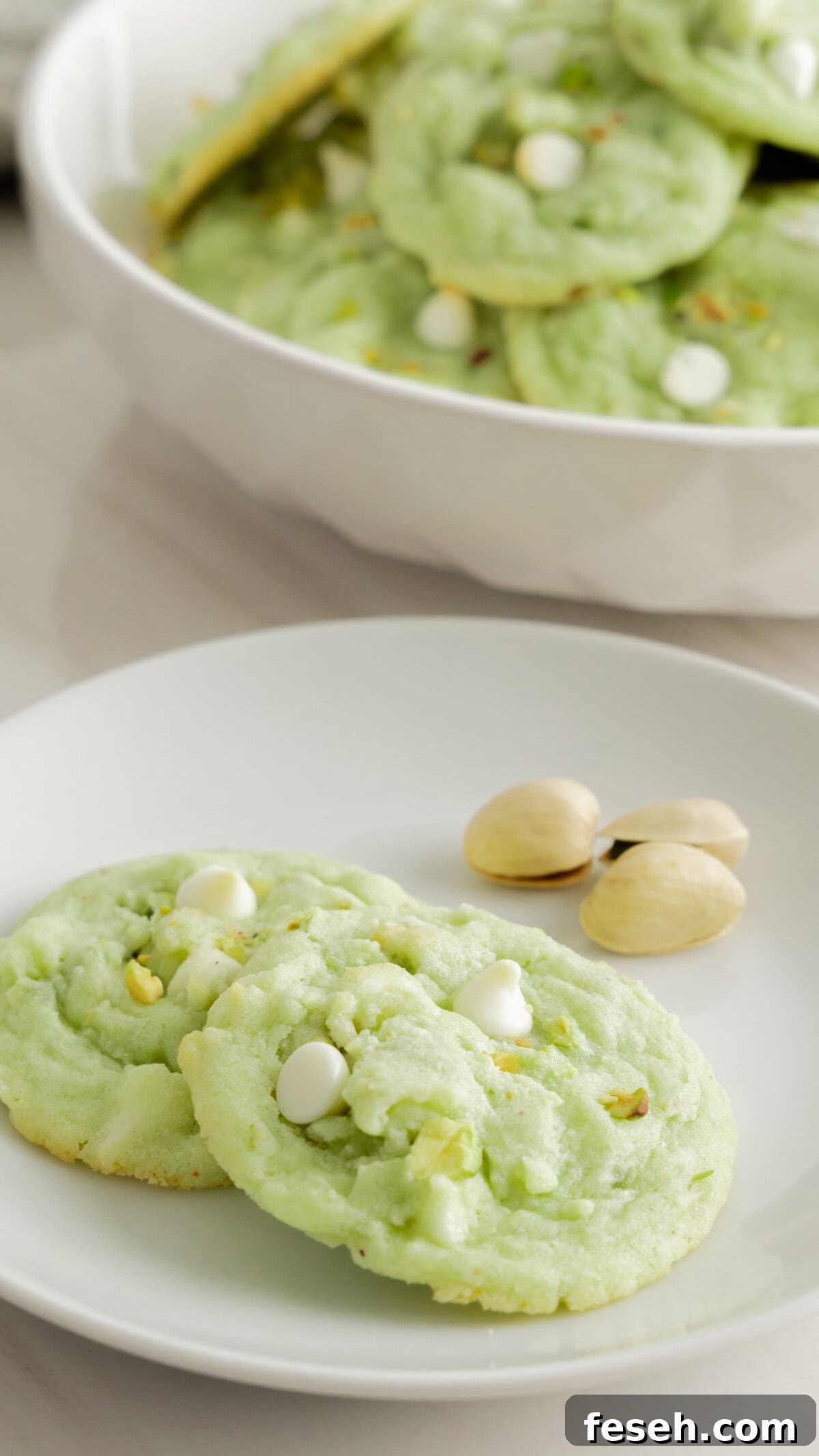 White plate with two pistachio cookies and three unshelled pistachios
