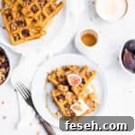 two triangles of waffles on a blue plate topped with a square of butter, a halved fig and granola.