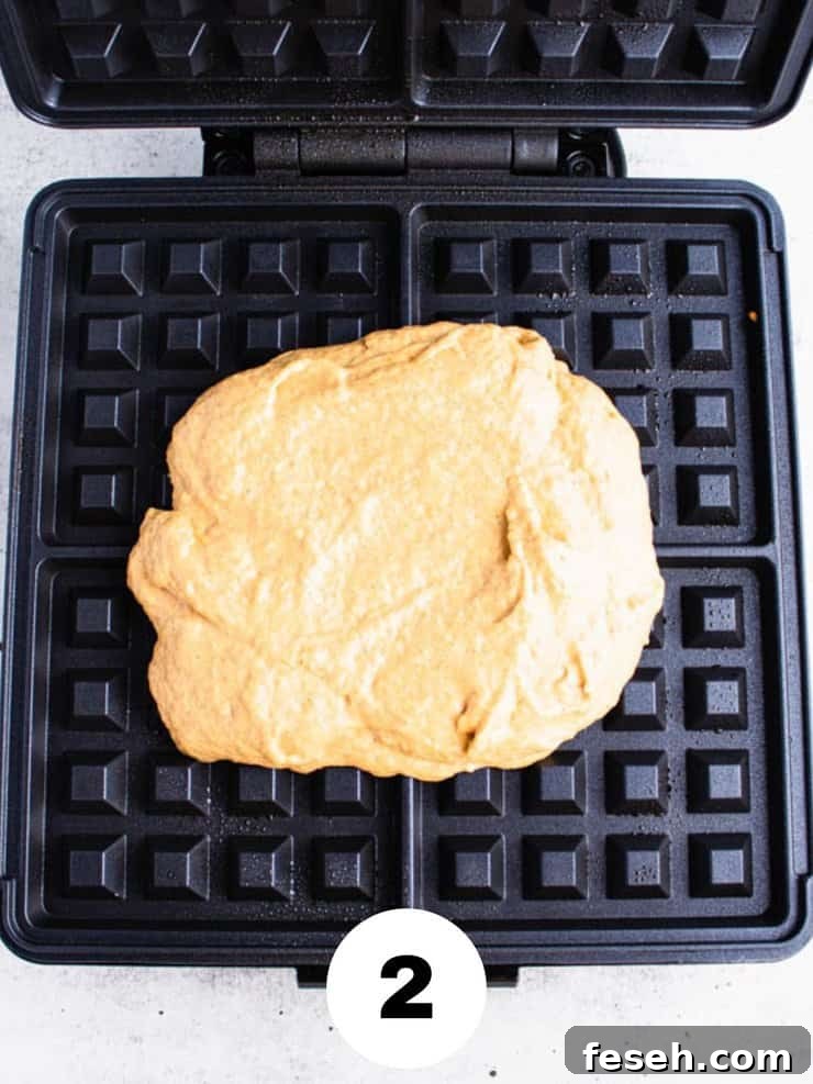Overhead view of light orange waffle batter on a black waffle iron.