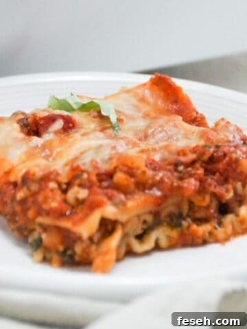 One serving of lasagna on a white plate with a napkin in front of the plate.
