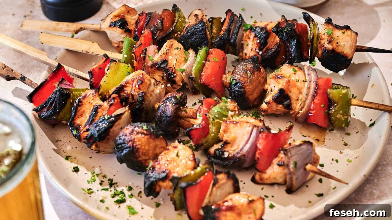 Grilled chicken skewers with red bell peppers, green bell peppers, and onions are served on a white plate, garnished with chopped herbs.