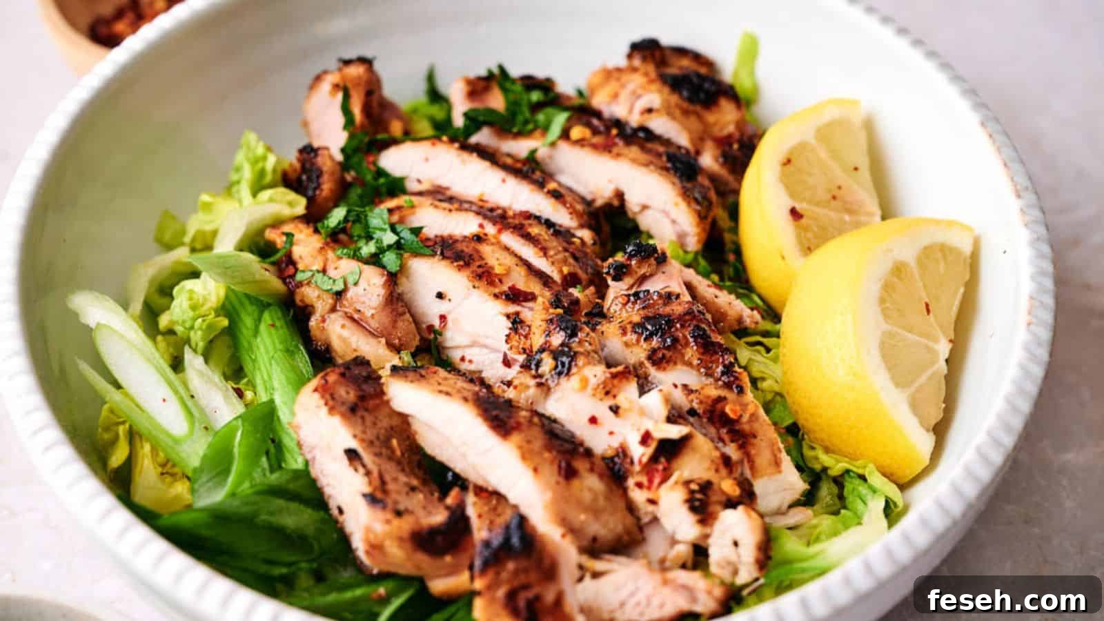 Grilled chicken breast slices served over a bed of greens with lemon wedges on the side.