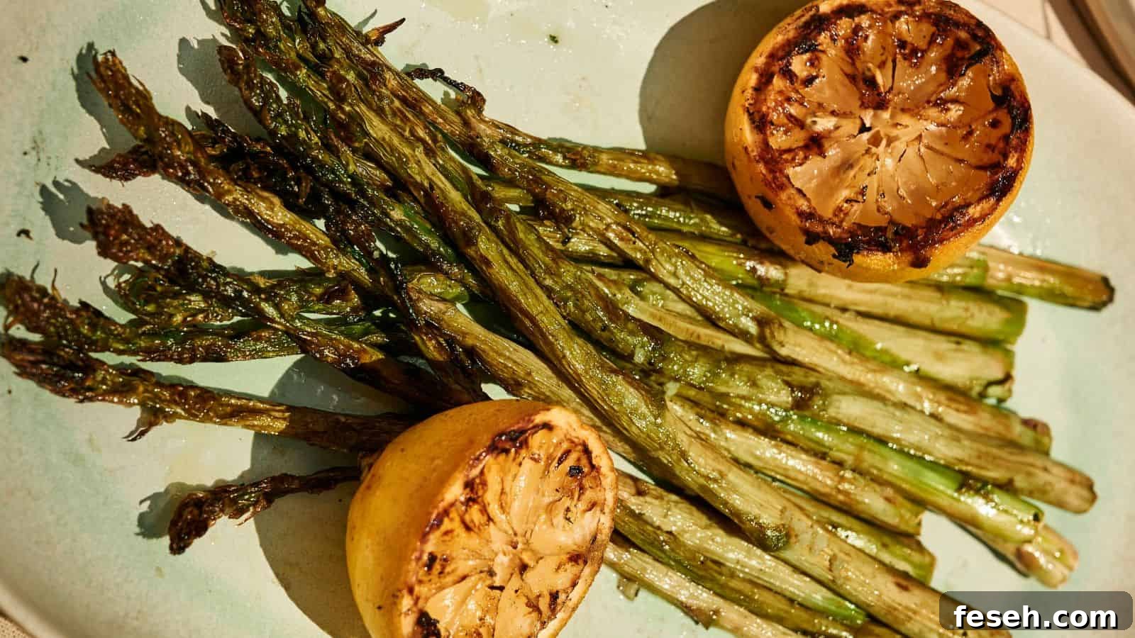 Grilled asparagus spears served on a plate with two charred lemon halves.