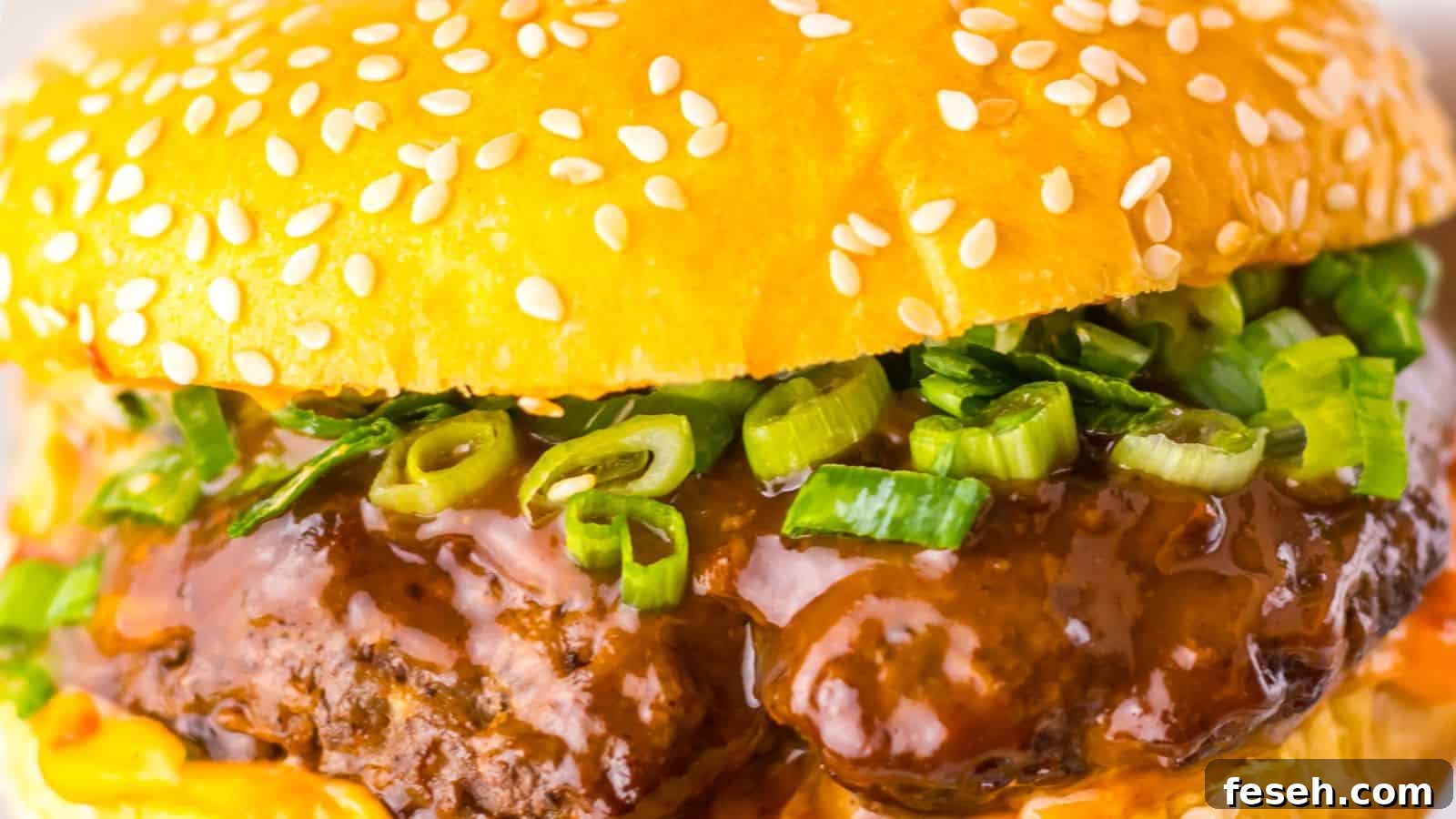 Close-up of a hamburger with a sesame seed bun, beef patty, green onions, and rich brown sauce.