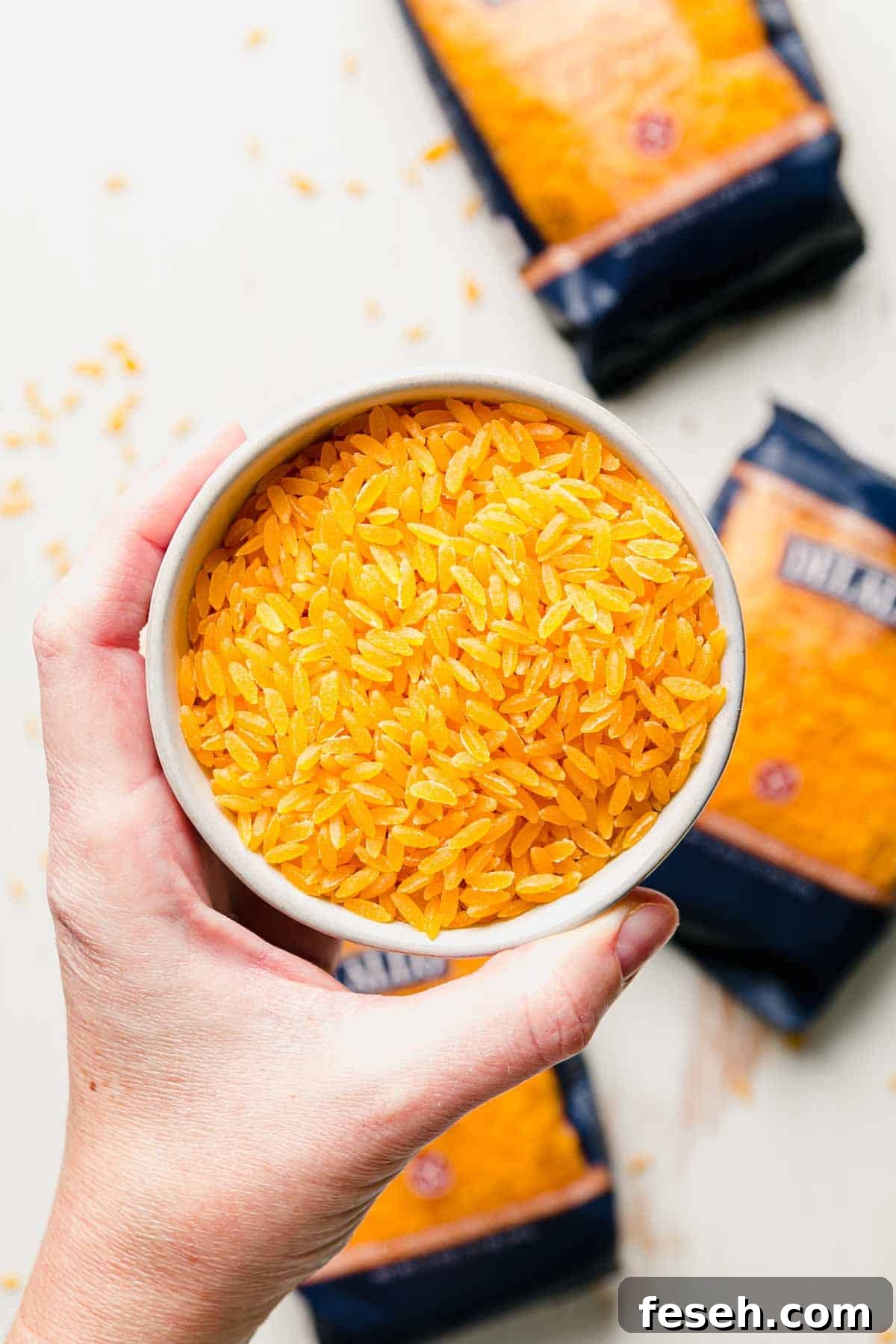 A small bowl of uncooked orzo held up by a hand.