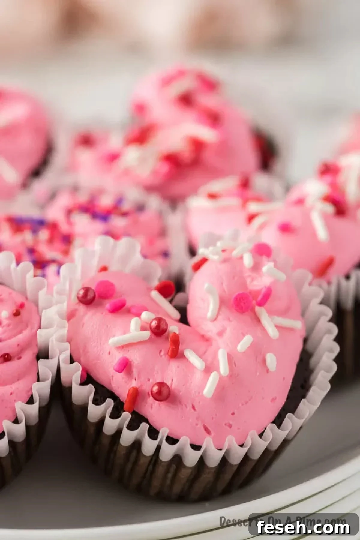 Close up of these chocolate heart cupcakes on a white plate topped with sprinkles.