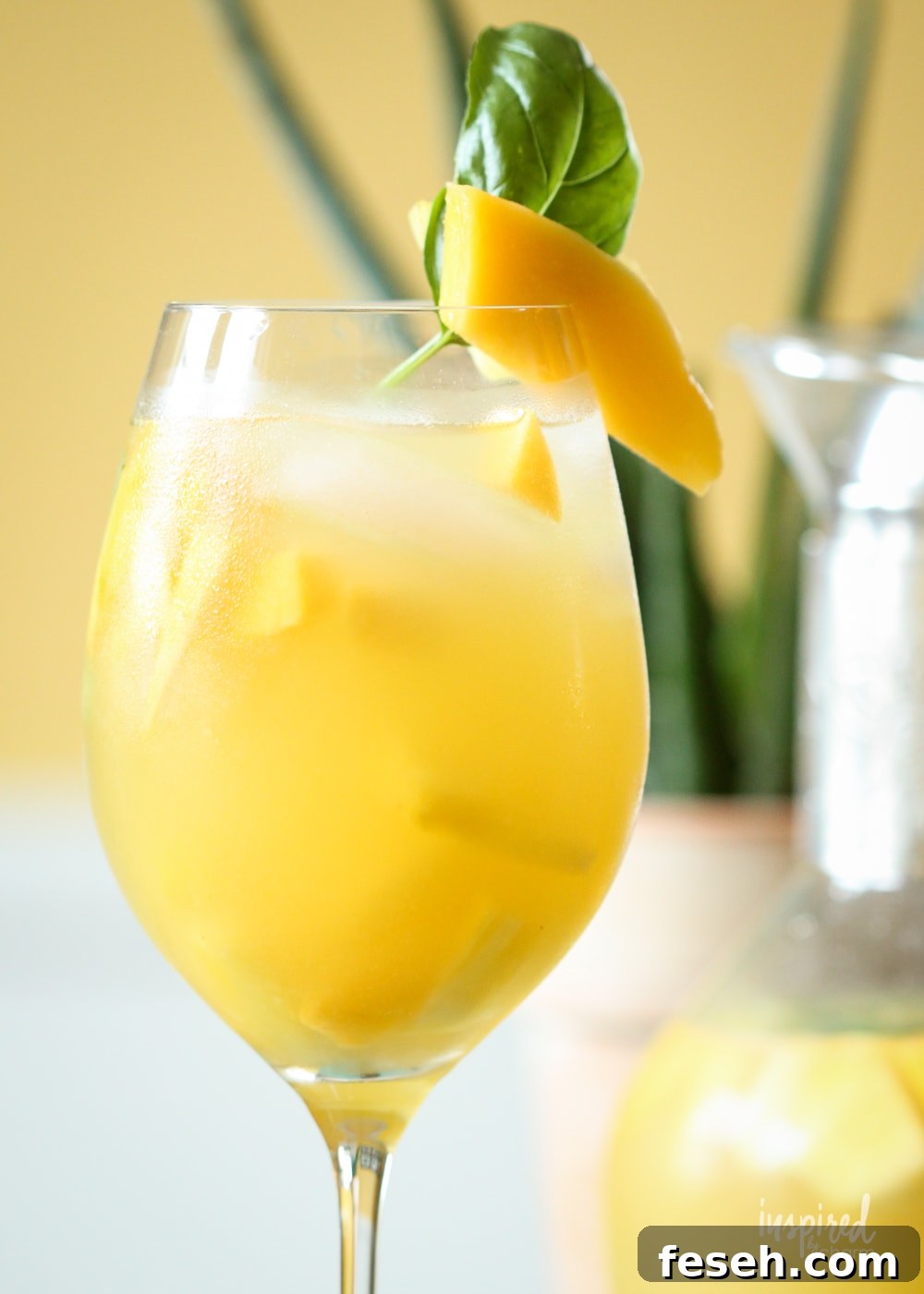 up close pineapple mango sangria in a glass with mango and basil garnish. 