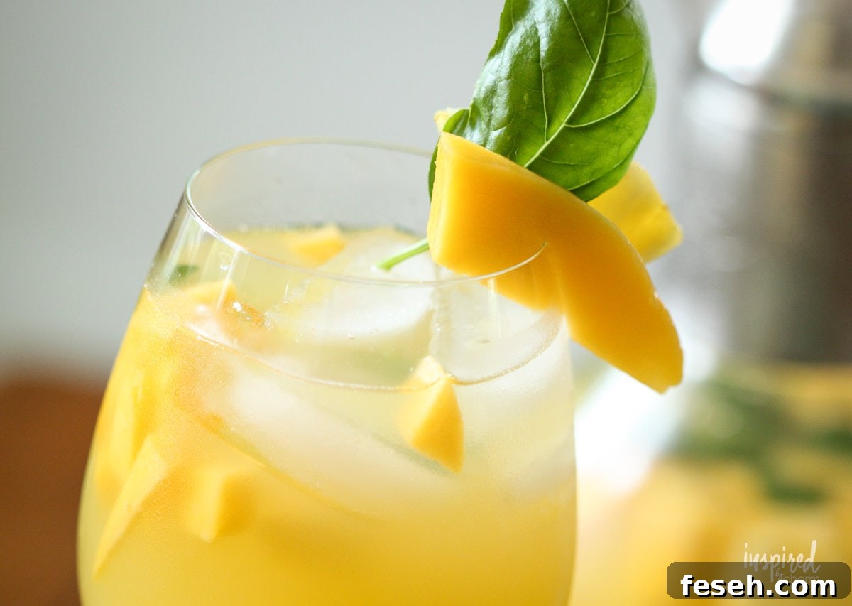 pineapple mango sangria in a glass with mango and basil garnish. 