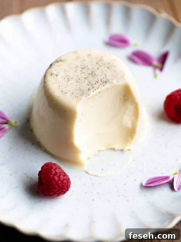 A vanilla panna cotta on a plate with a bite out and raspberries at the side.