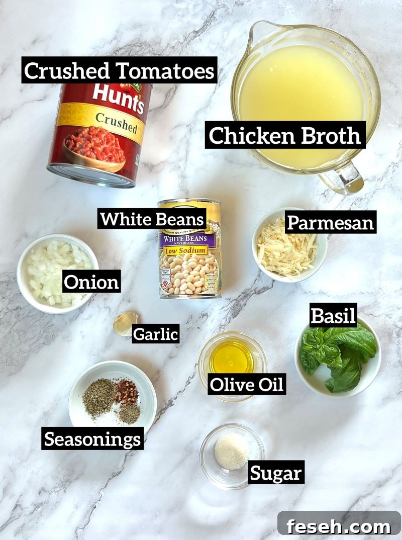 Ingredients displayed for tomato soup with white beans. Canned crushed tomatoes, chicken broth, white beans, onion, garlic, parmesan cheese, olive oil, basil, Italian seasoning, red pepper flakes, salt and pepper, sugar. 