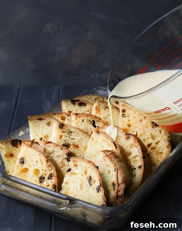panattone sliced arranged in a baking pan with custard being poured on top
