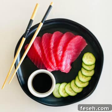 tuna sashimi recipe fully prepared on plate with soy sauce, sliced cucumbers and chopsticks.