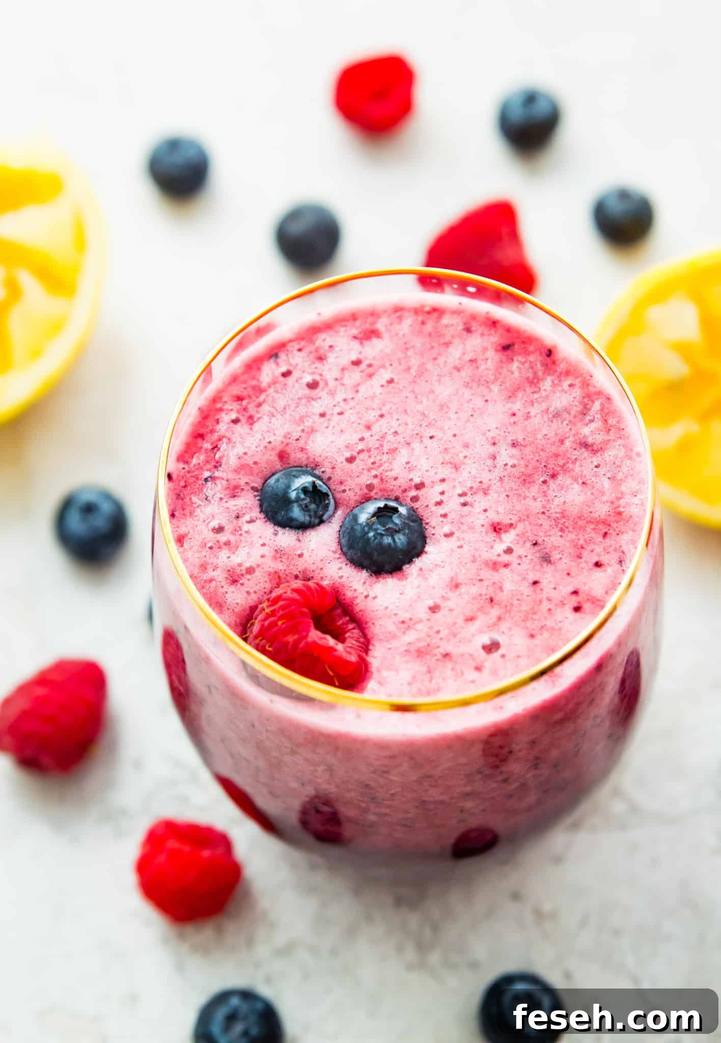 A berry lemonade smoothie in a glass with a raspberry and blueberries on top.