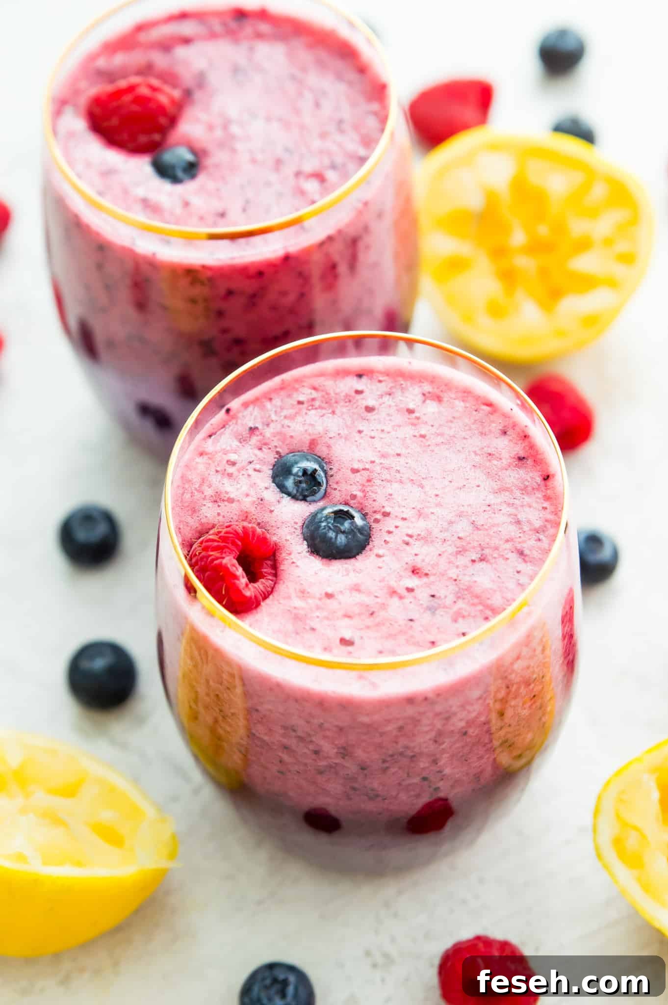 Two glasses of lemonade smoothie topped with blueberries and raspberries. 