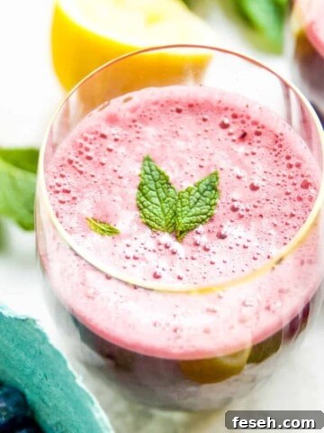 A glass of blueberry mint lemonade garnished with mint leaves.