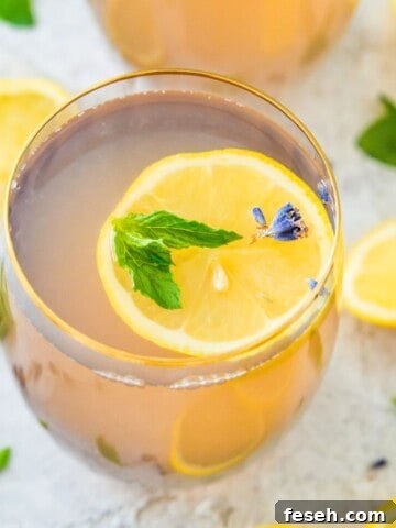 A glass of lavender mint lemonade topped with a lemon slice, mint leaves and lavender flowers.