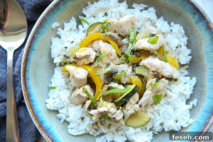 A bowl of Thai basil chicken with rice and a spoon lying on a cloth napkin on the left of the bowl.