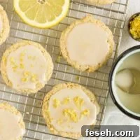 Almond flour lemon cookies topped with a glaze on a rectangular wire cooling rack with slices of lemon placed on the rack.