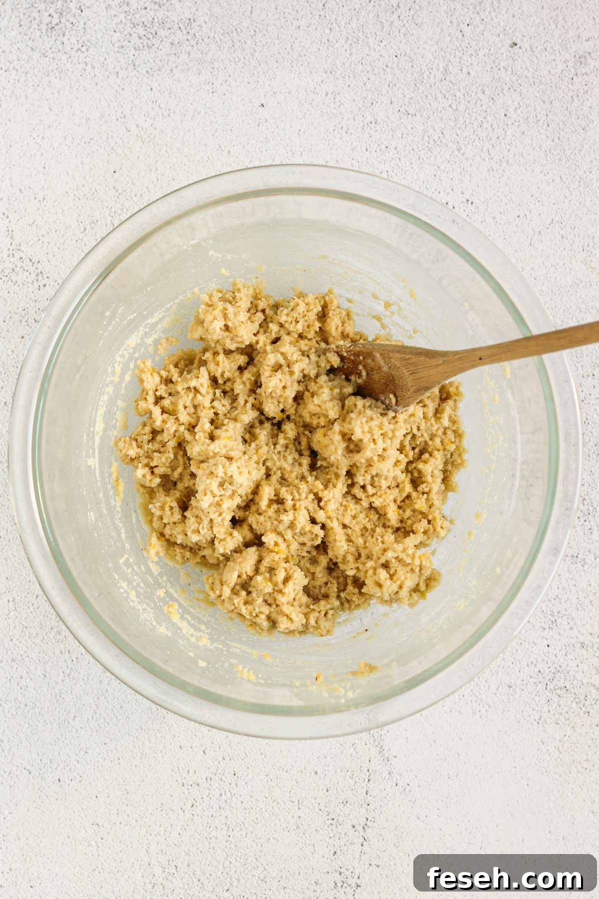 Almond flour lemon cookie dough mixed in a glass mixing bowl with a wooden spoon in the bowl.