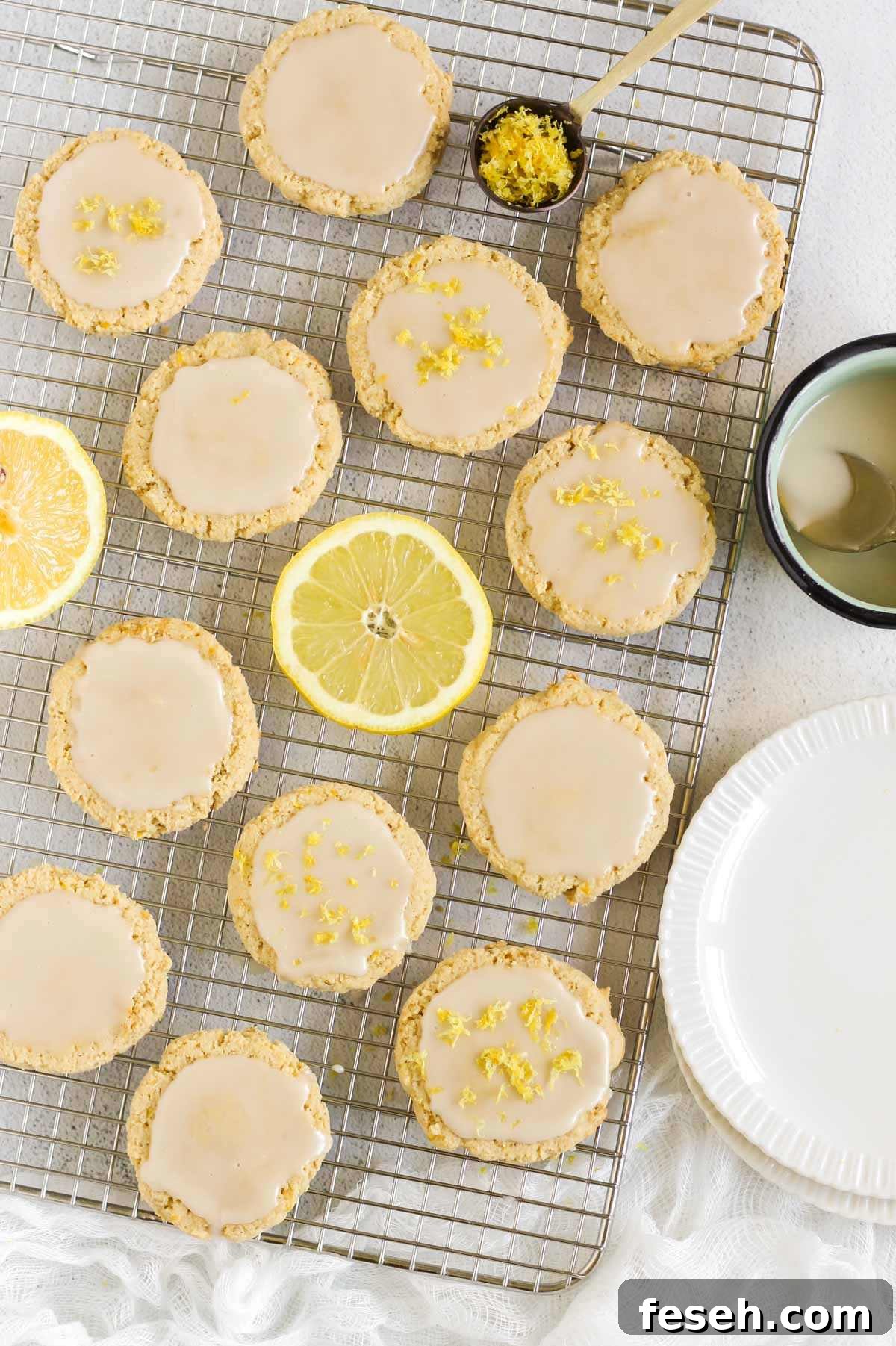 Almond flour lemon cookies topped with a glaze on a rectangular wire cooling rack with slices of lemon placed on the rack.