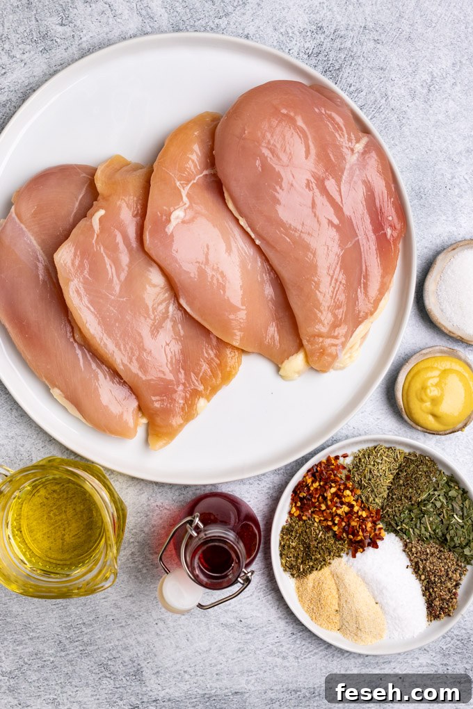 Overhead ingredient shot of chicken breast, avocado oil, red wine vinegar, Italian spices, Dijon mustard, and sugar.