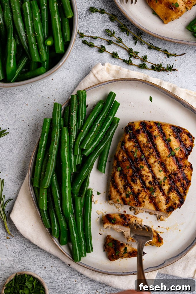Overhead shot of Italian marinated chicken with a slice taken out of the chicken, and a fork is holding the slice of chicken. Green beans are on the plate next to the chicken.