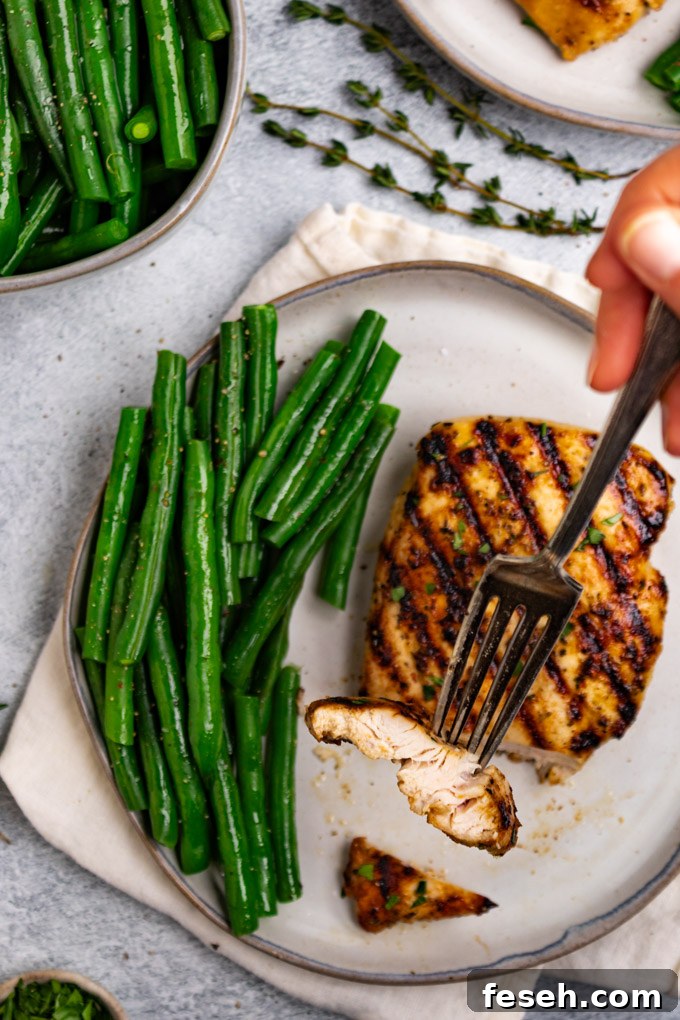 Overhead shot of Italian marinated chicken with a slice of chicken on a fork, being help up close to the camera. Green beans are on the plate, next to the chicken.