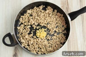 Picture of a skillet with ground chicken, minced garlic and ginger.