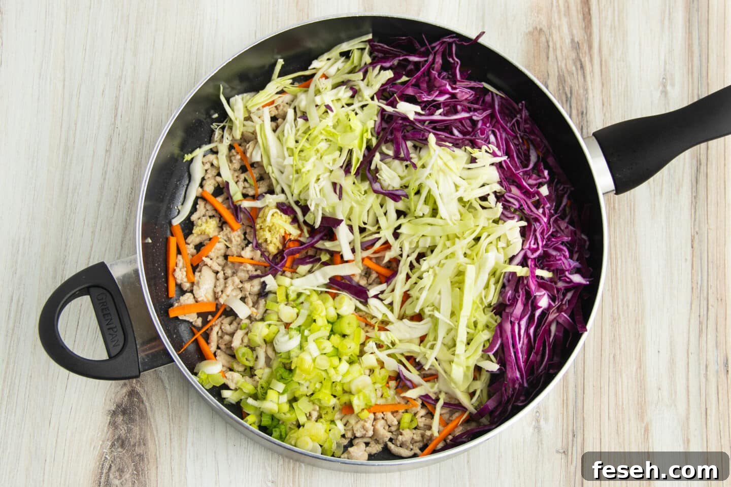 Picture of a skillet with added cabbage, carrots and green onions.