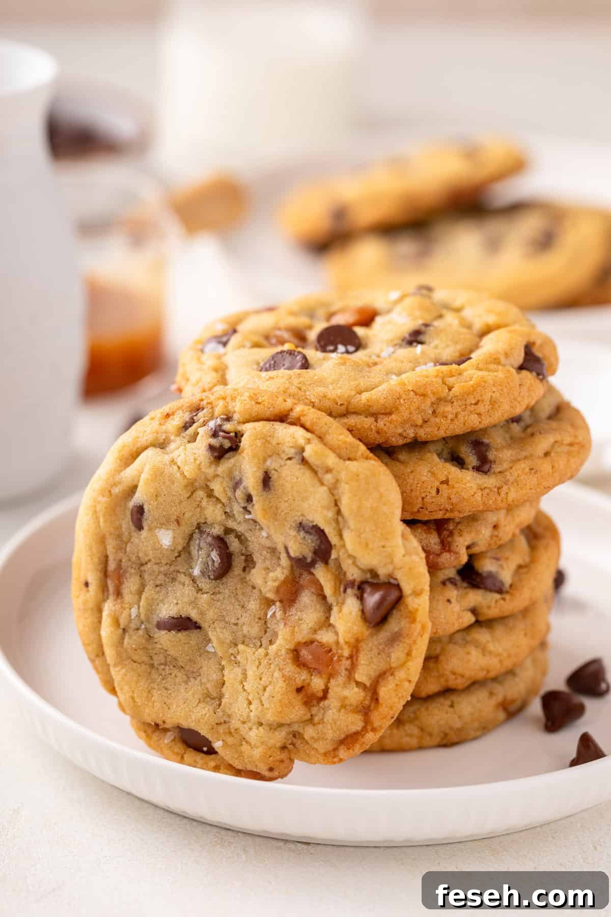Salted caramel chocolate chip cookie leaning against a stack of the cookies on a white plate.
