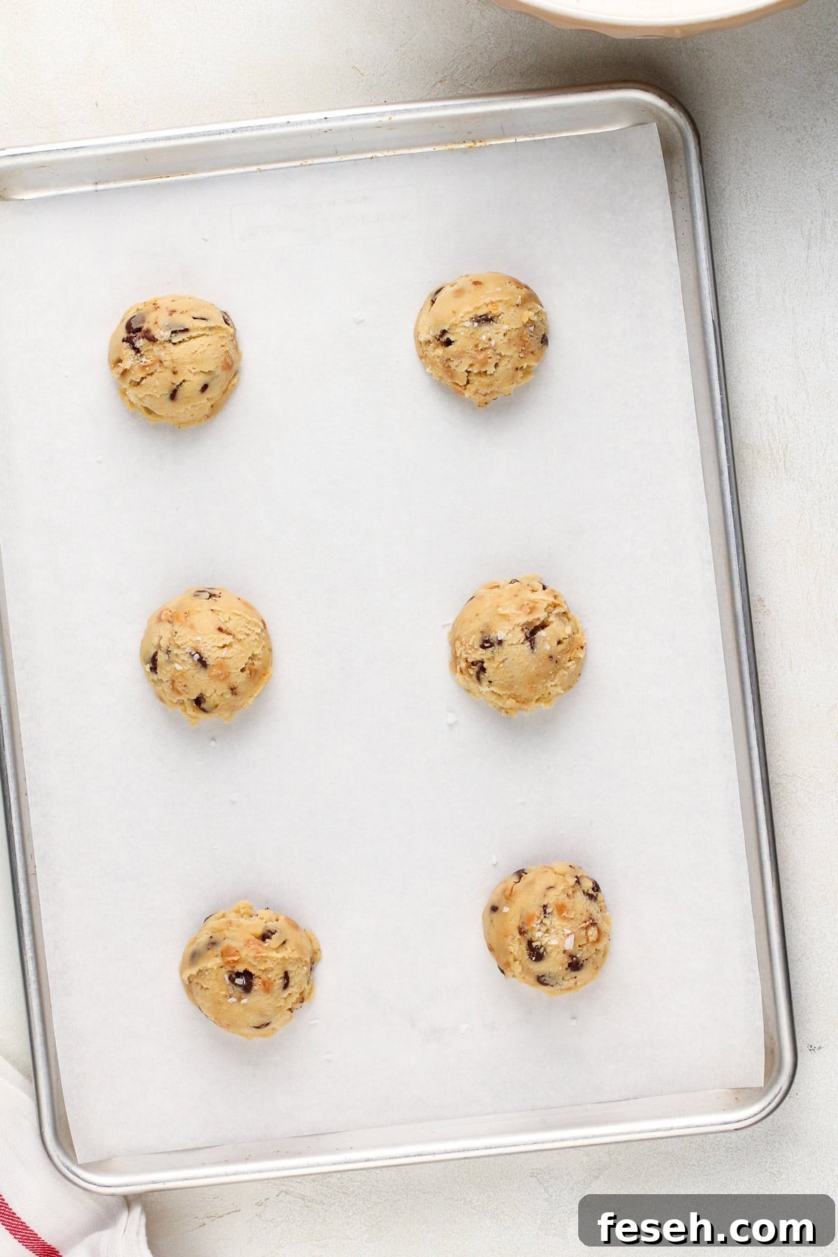 6 balls of salted caramel chocolate chip cookie dough on a lined baking sheet, ready to be baked.