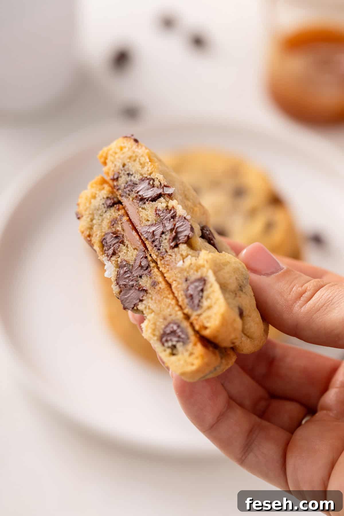 Hand holding up a halved salted caramel chocolate chip cookie.