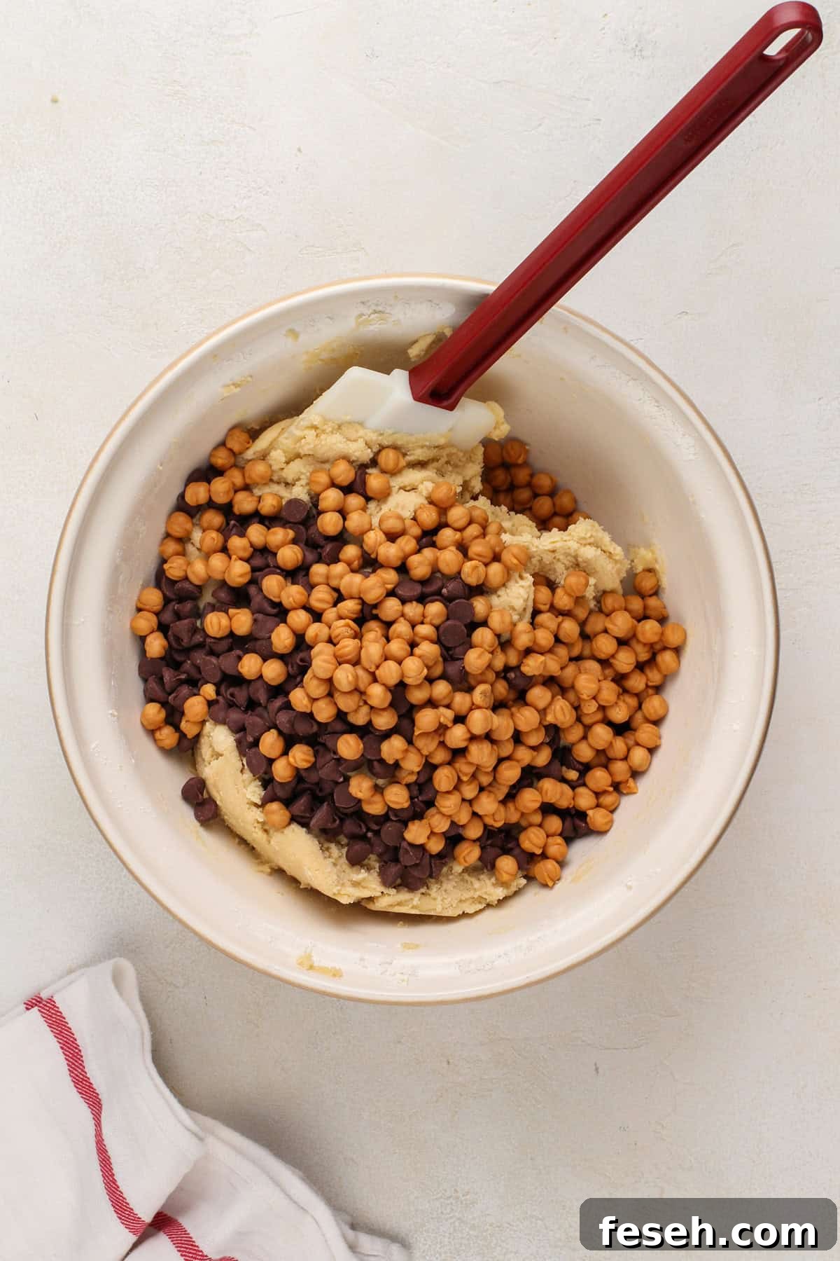 Chocolate chips and caramel bits being added to cookie dough in a mixing bowl.