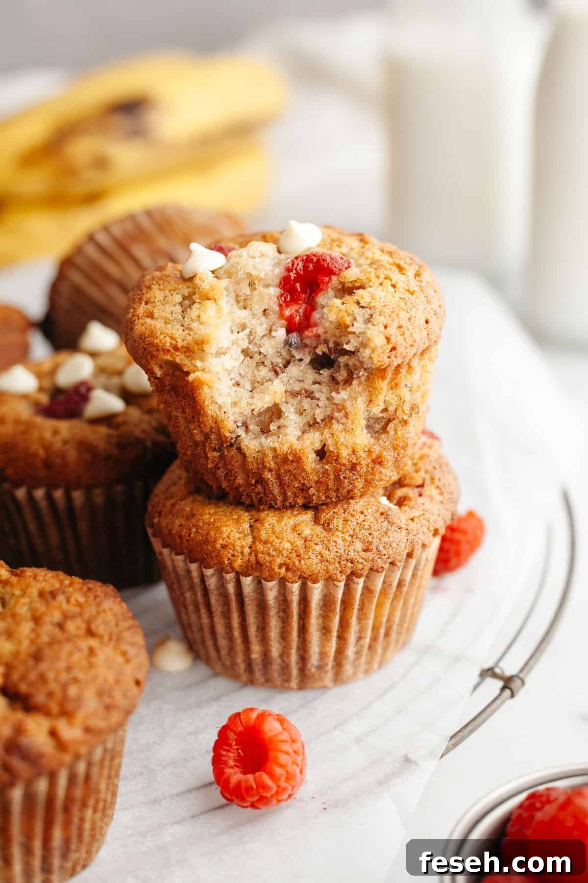 Two raspberry banana muffins stacked on top of each other, one has a bite taken out of it.