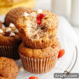 Two raspberry banana muffins stacked on top of each other, one has a bite taken out of it.