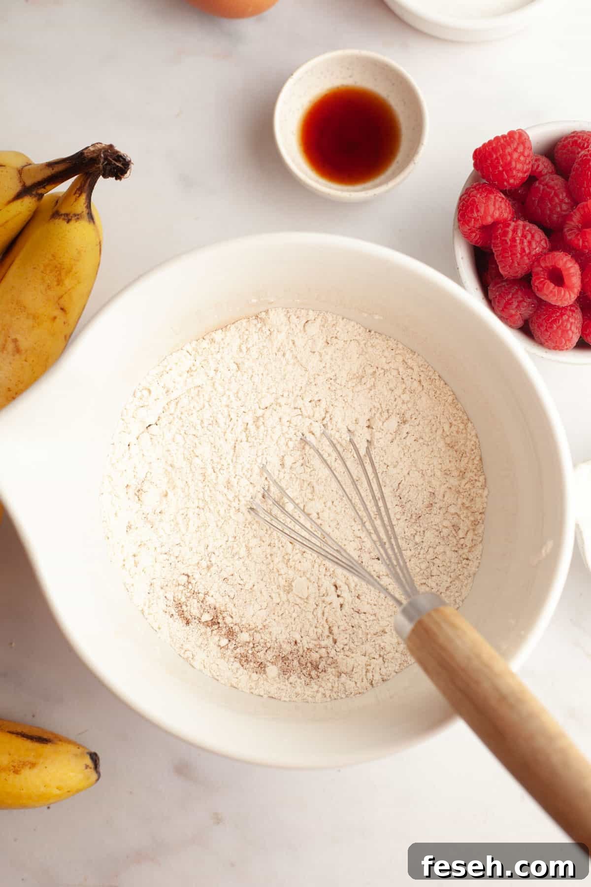 A white bowl with a whisk and flour in it.