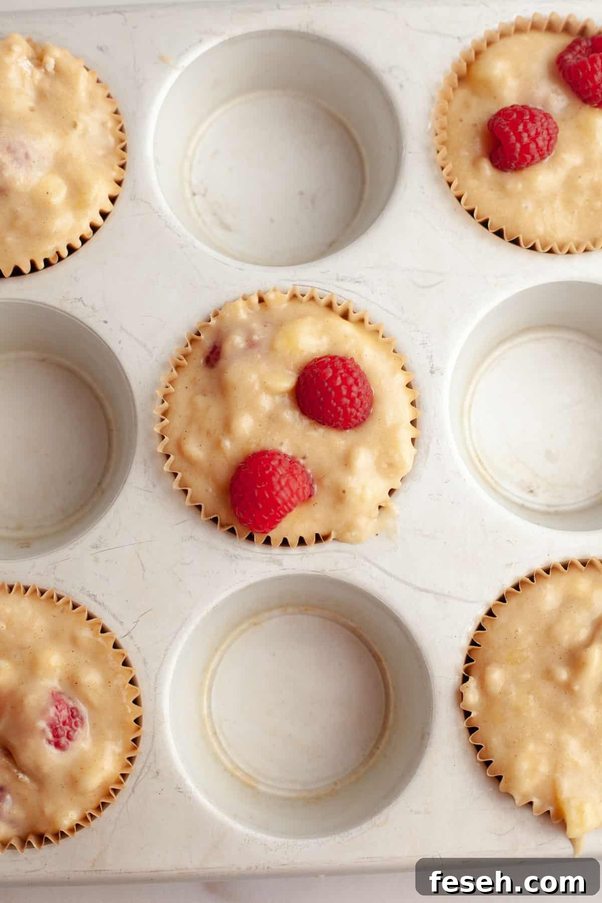 Unbaked banana raspberry muffins in a muffin pan.