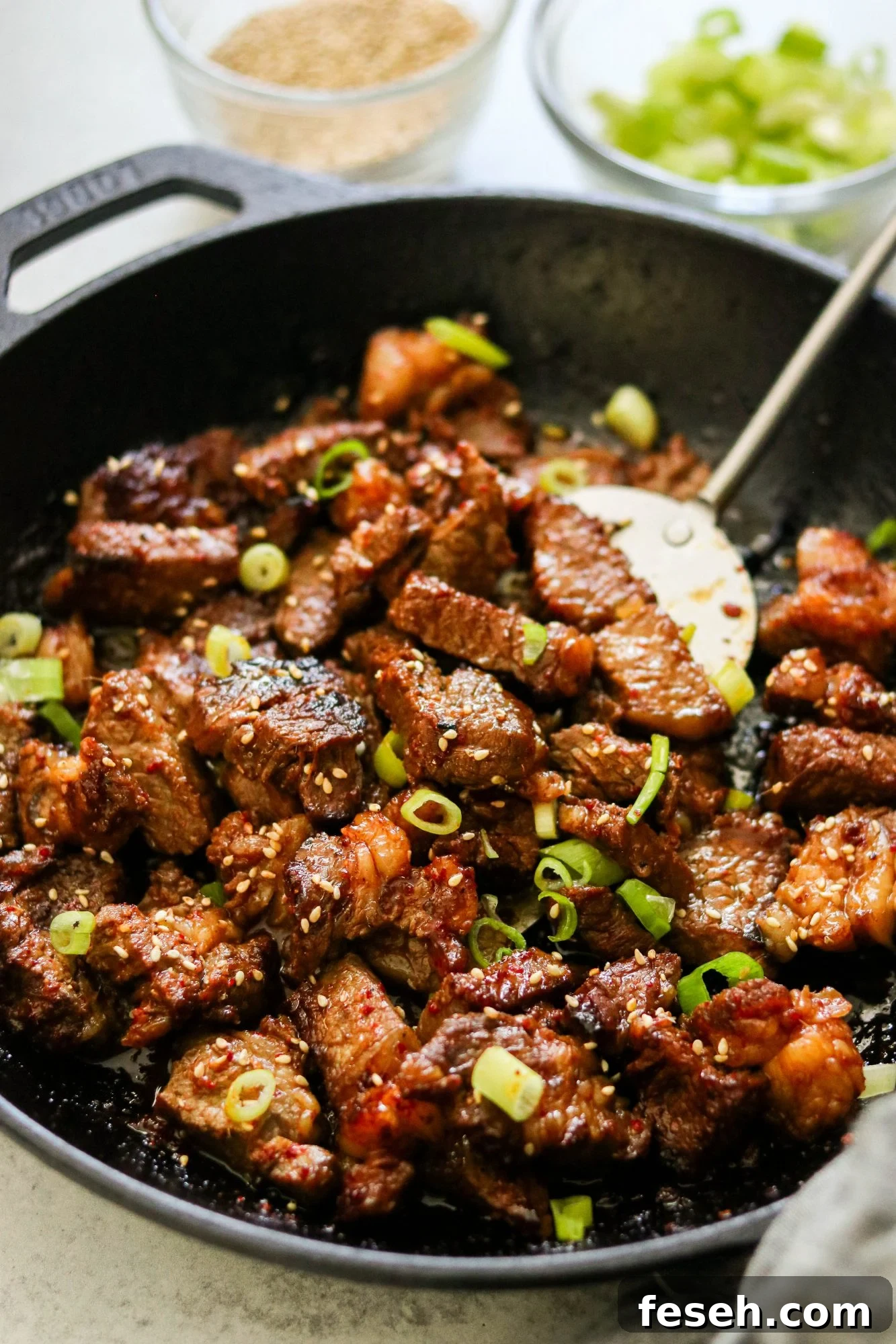 Skillet of seared Korean steak bites topped with sesame seeds and scallions.