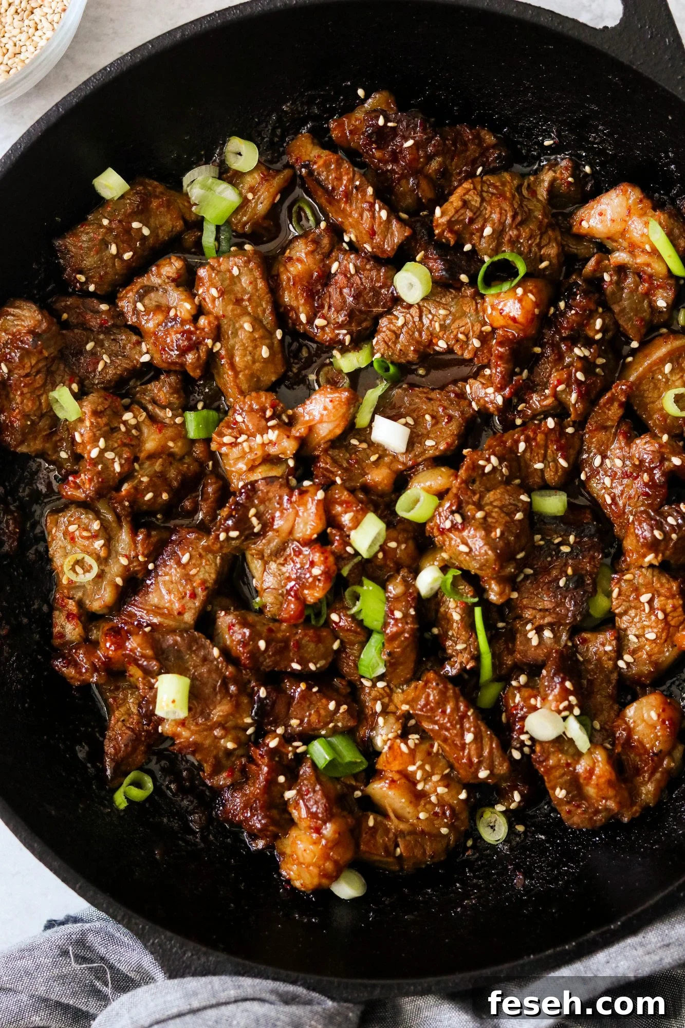Close-up of bulgogi-style steak bites in a skillet with sesame seeds and scallions.