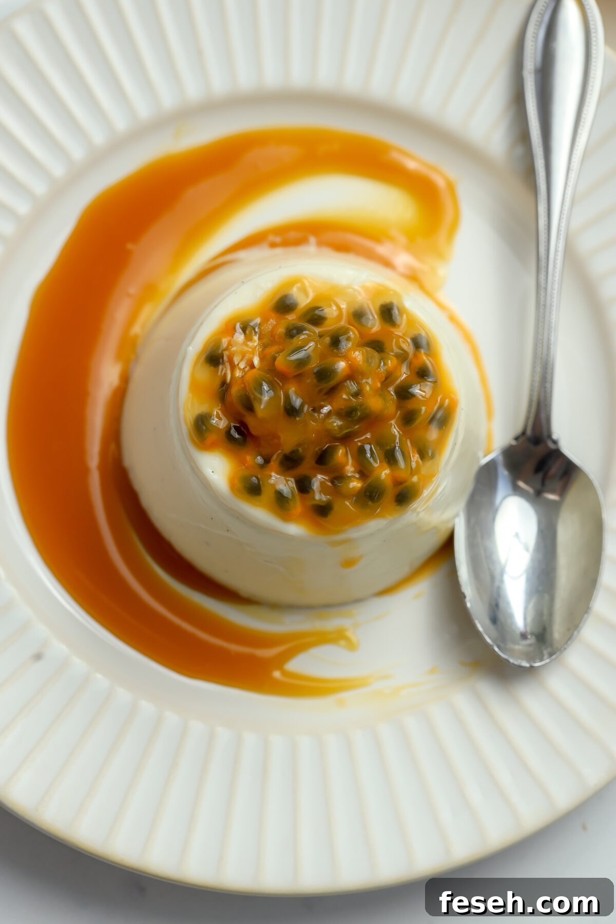 A top view of a creamy smooth Panna Cotta with a passion fruit caramel topping with a spoon next to it.