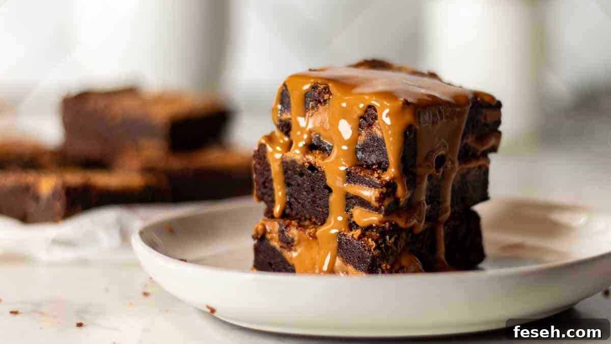 Drizzling Biscoff spread over a stack of Biscoff brownies with a backdrop of more brownies, perfect for a tutorial on making Biscoff brownies.