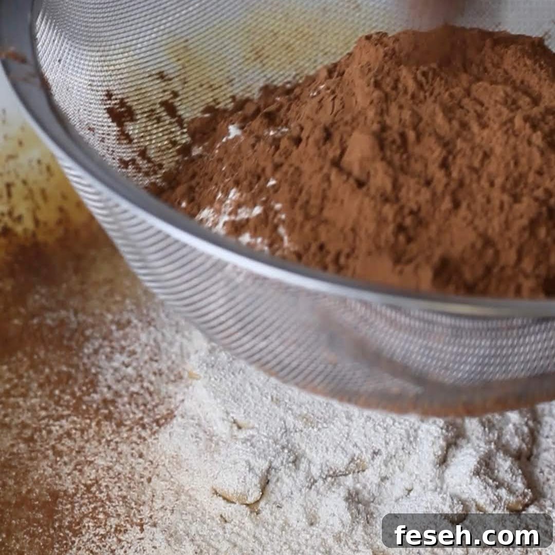 Sifting dry ingredients for biscoff brownies, with cocoa powder and flour creating a fine, lump-free mixture, an essential step for baking.