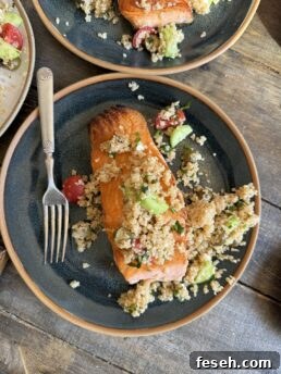a photo of salmon on a blue plate with greek quinoa salad on top and a fork next to it