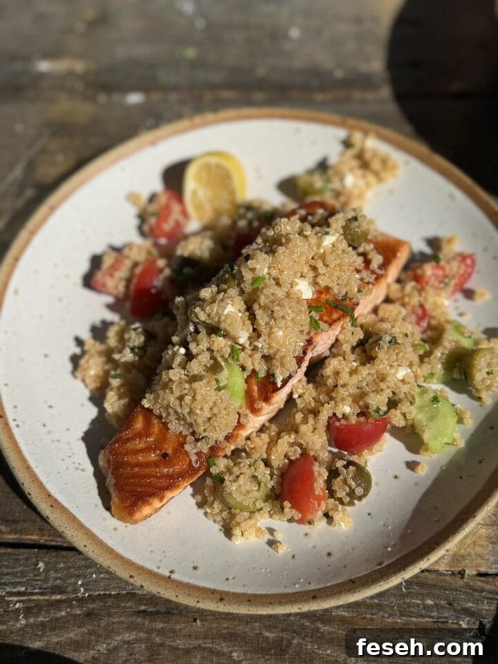a three quarter view photo of salmon with greek quinoa salad on it on a white speckled plate